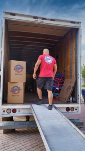 A mover walks up a ramp into a Skyway Moving & Storage truck, surrounded by packed boxes and equipment.